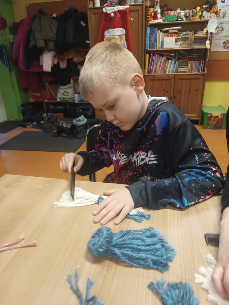 Uczeń podczas warsztatów przy stoliku wykonują pracę z wykorzystaniem włóczki 