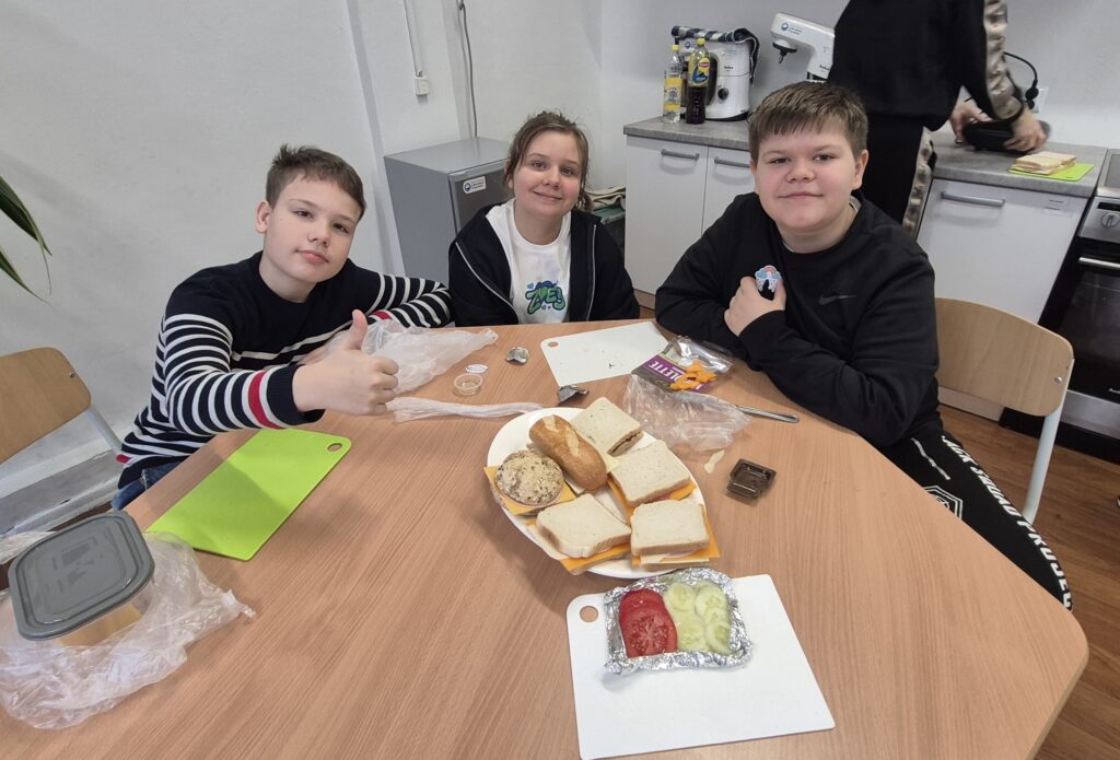 Uczniowie i uczennica IV a siedzą przy stole w Kuchcikowie, po środku stołu talerz pełen zrobionych przez nich kanapek.