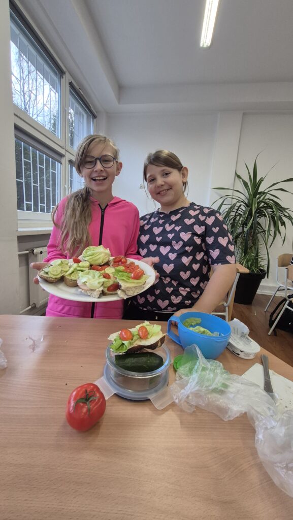 Dwie uczennice trzymające talerz pełen kolorowych kanapek.