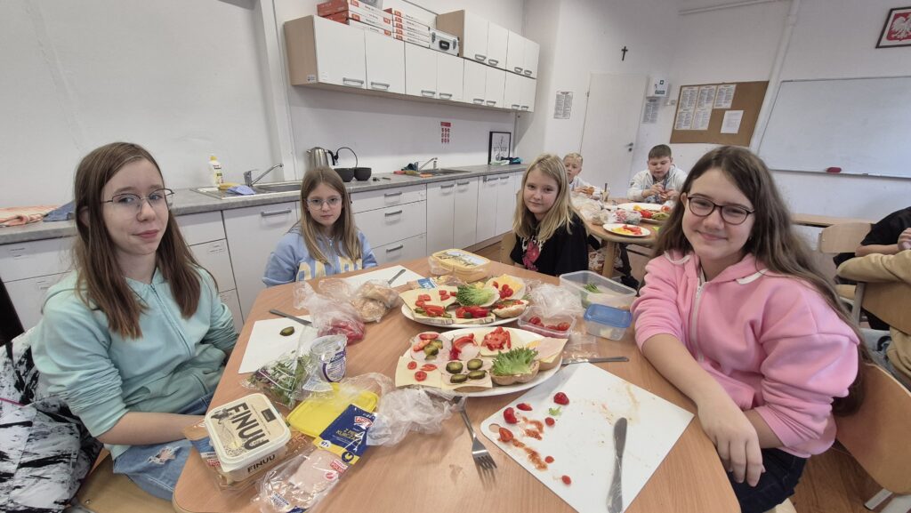 Na pierwszym planie dwa talerze pełne kolorowych kanapek a dalej dwie uczennice IVa autorki tych kanapek.