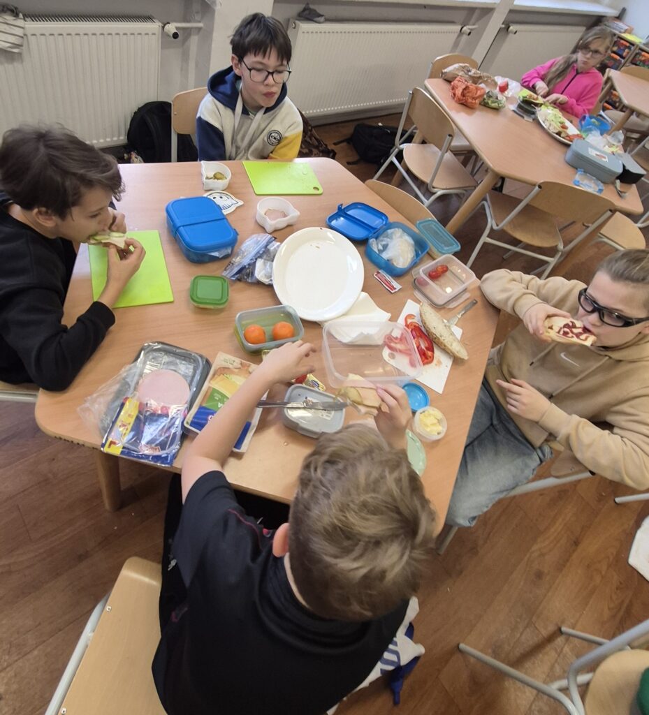 W Kuchcikowie stolik zastawiony talerzykami, pojemnikami z jedzeniem. Uczniowie IVa mają przed sobą zielone deski do krojenia.