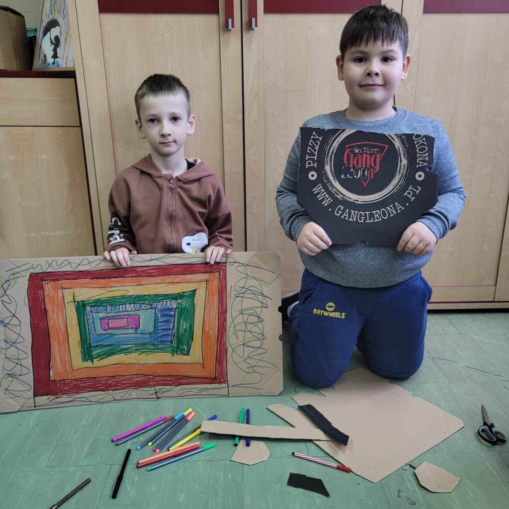 dwóch chłopców pokazuje swoje prace wycięte z pudełek i pomalowane. 