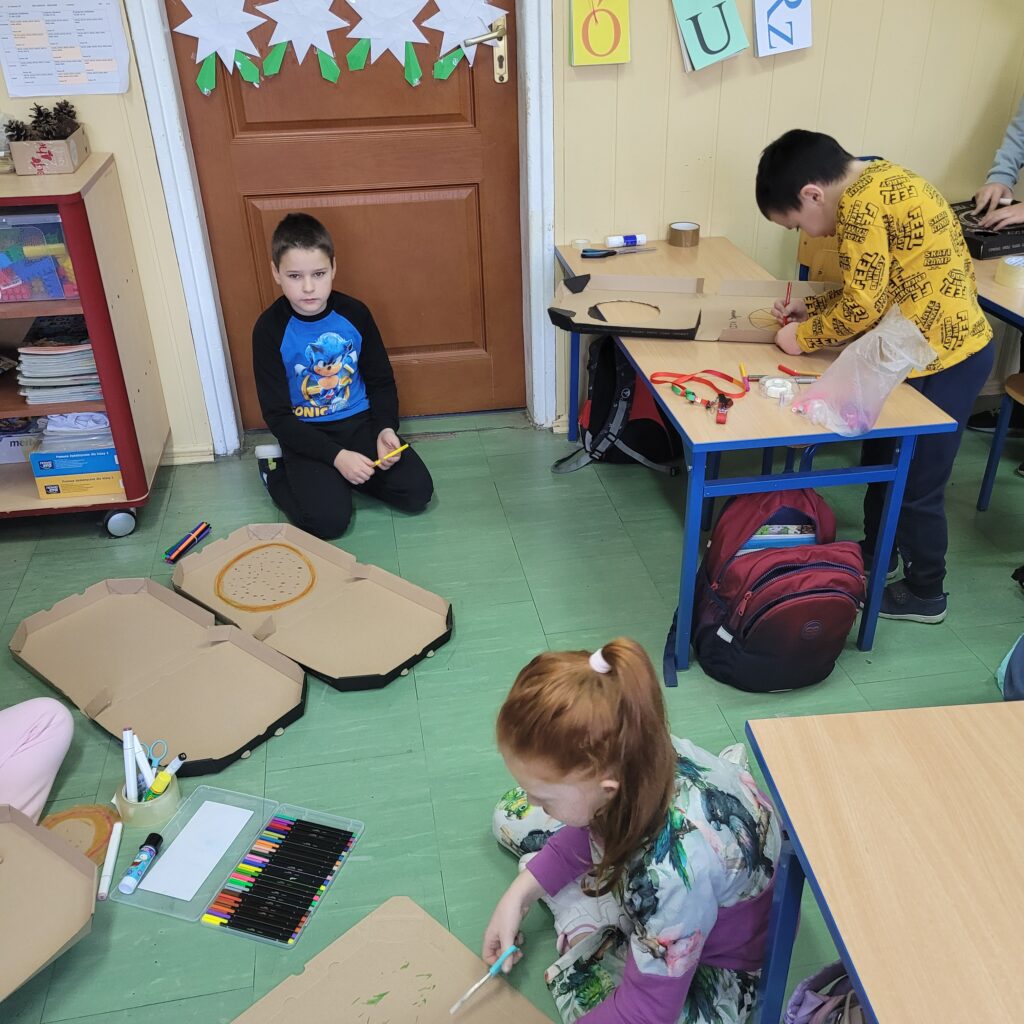 widać jak uczniowie wykonują prace. Na podłodze i przy ławkach.