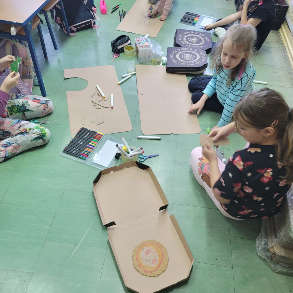 dzieci siedzą na podłodze i wycinają z pudełek prace.