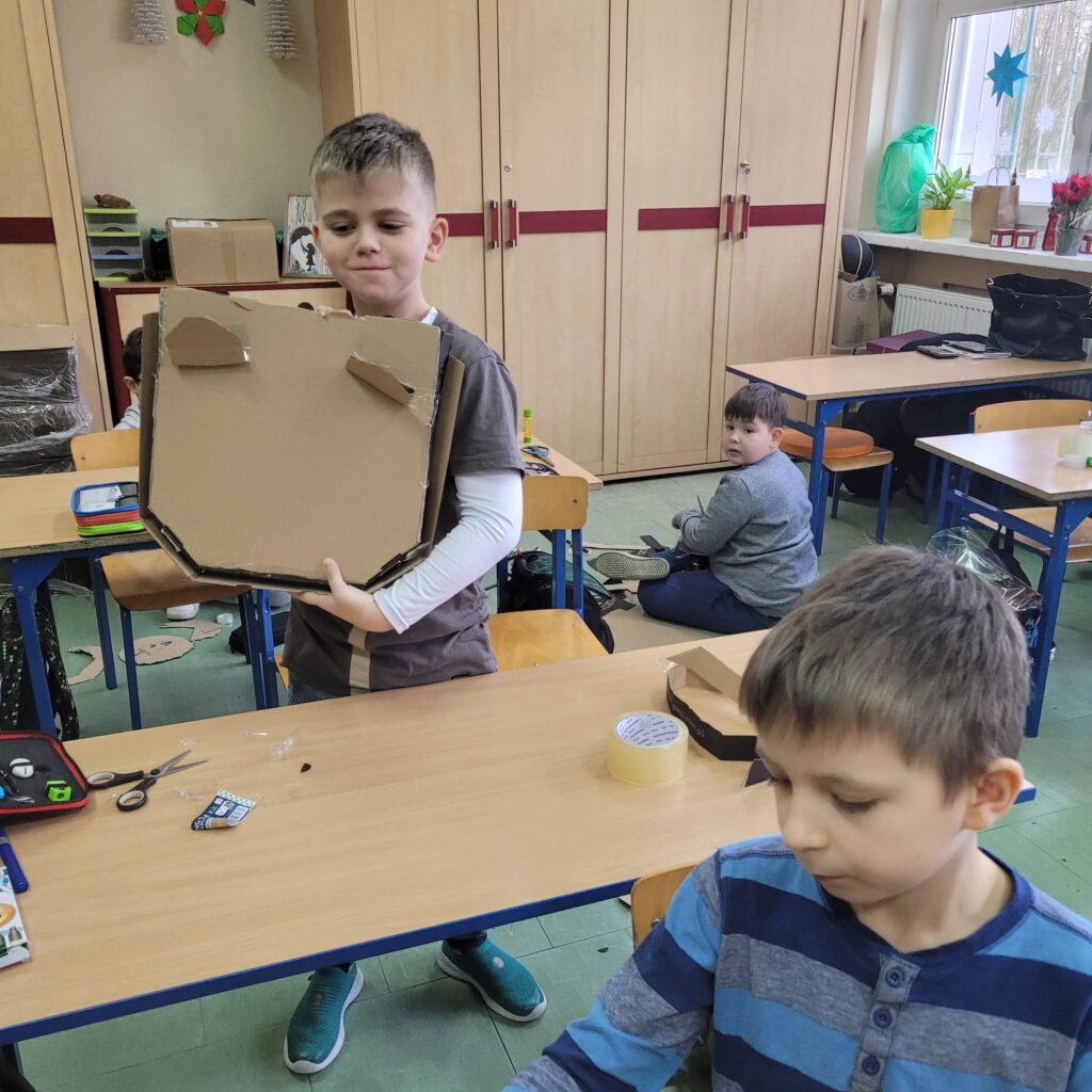 uczeń trzyma pudełko po pizzie ozdobione przez siebie, widać pudełko z przymocowanymi uszami