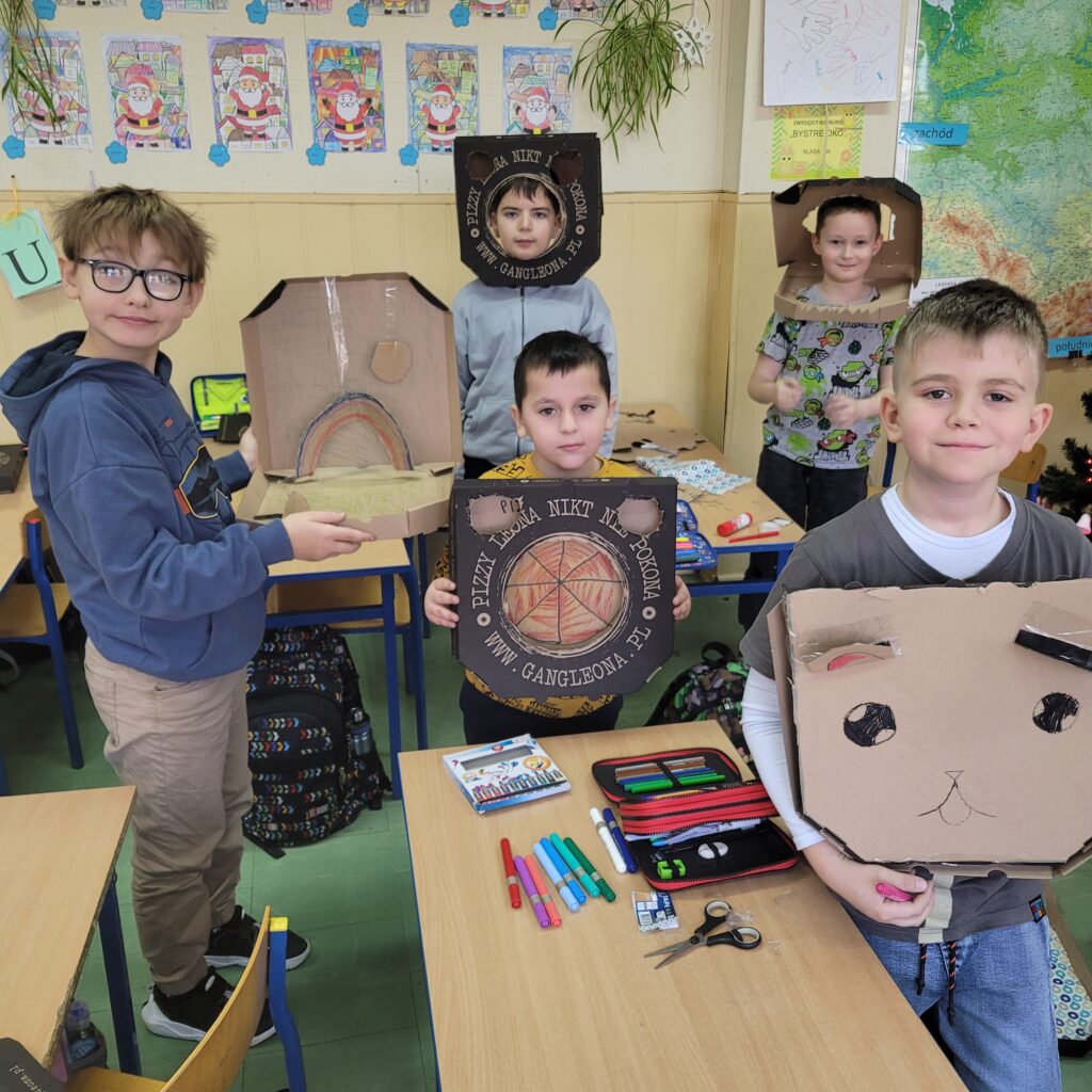 widzimy grupę uczniów trzymających swoje kolorowe prace wykonane z pudełek po pizzie