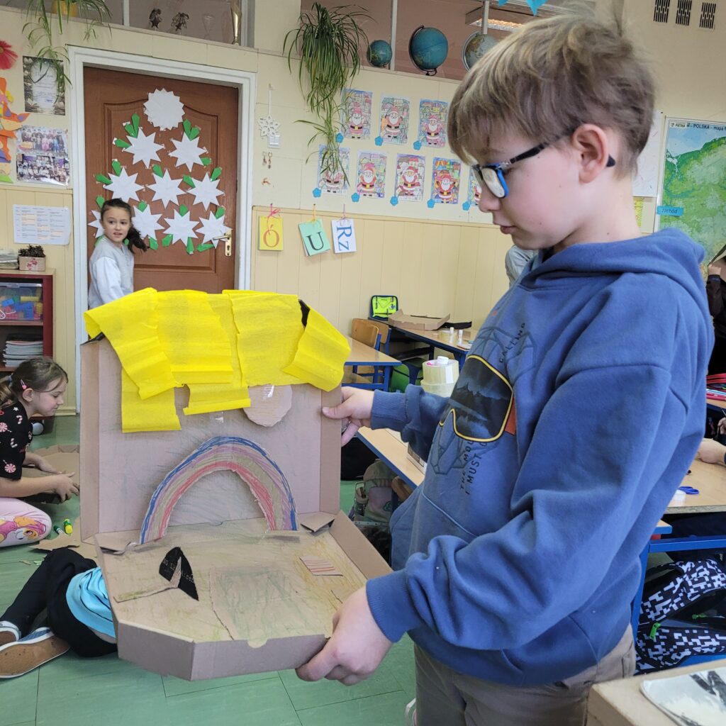 uczeń trzyma pudełko po pizzie ozdobione przez siebie, widać tęczę