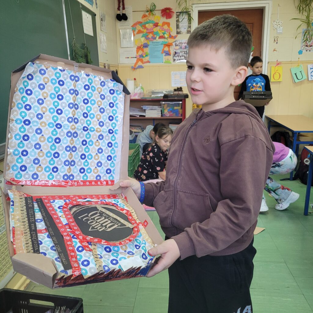 uczeń trzyma pudełko po pizzie ozdobione przez siebie, widać kolorowe papiery