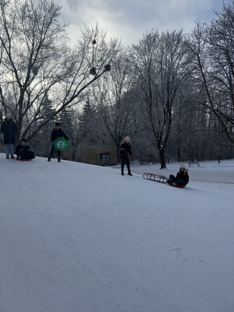 Uczniowie klasy 6b podczas wfu na śniegu zjeżdżają z górki.