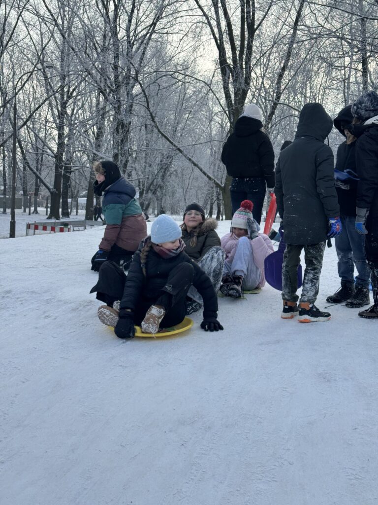 Uczniowie klasy 6b podczas wfu na śniegu zjeżdżają z górki.