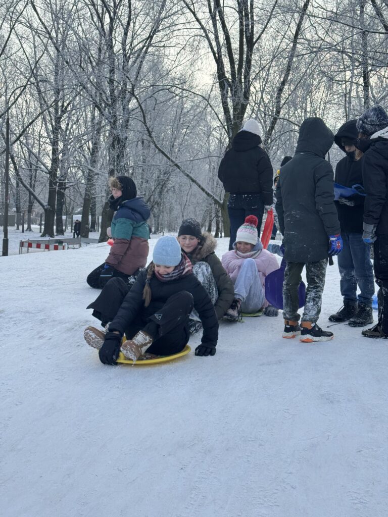Uczniowie klasy 6b podczas wfu na śniegu zjeżdżają z górki.