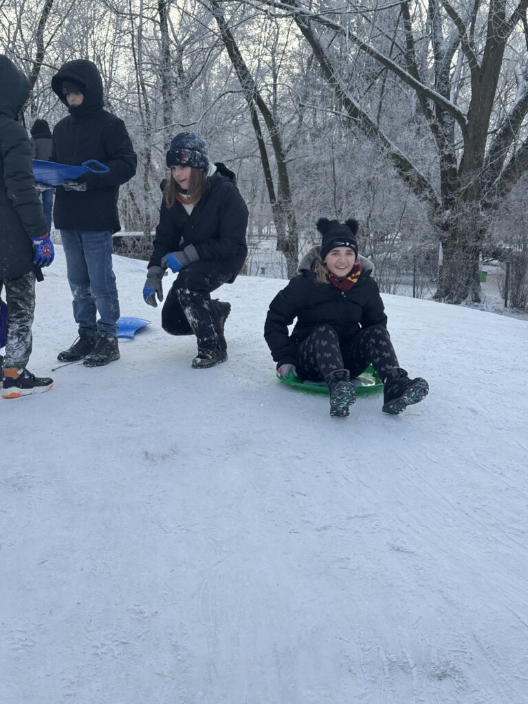 Uczniowie klasy 6b podczas wfu na śniegu zjeżdżają z górki.