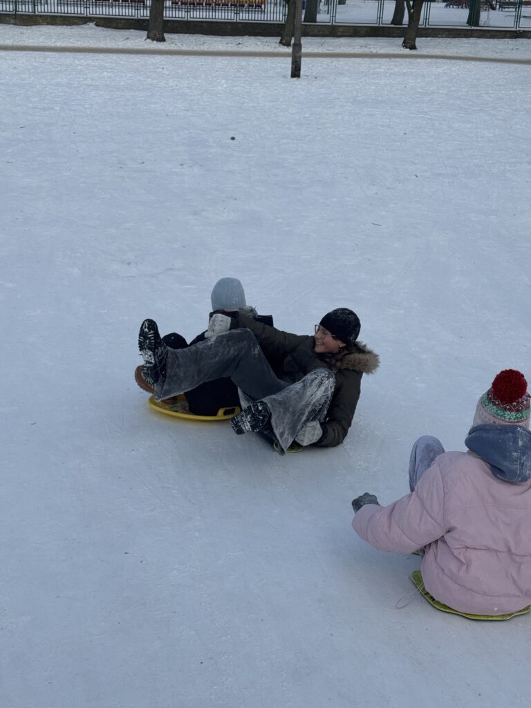 Uczniowie klasy 6b podczas wfu na śniegu zjeżdżają z górki.