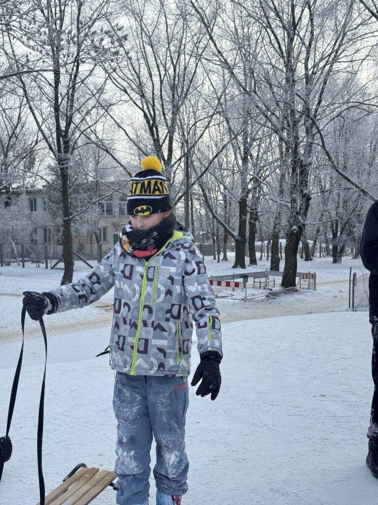 Uczeń klasy 6b podczas wfu na śniegu stoi pod górką z sankami.