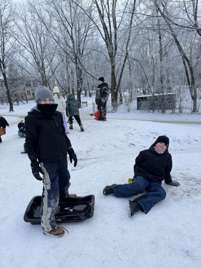 Uczniowie klasy 4b podczas wfu na śniegu zjeżdżają z górki.