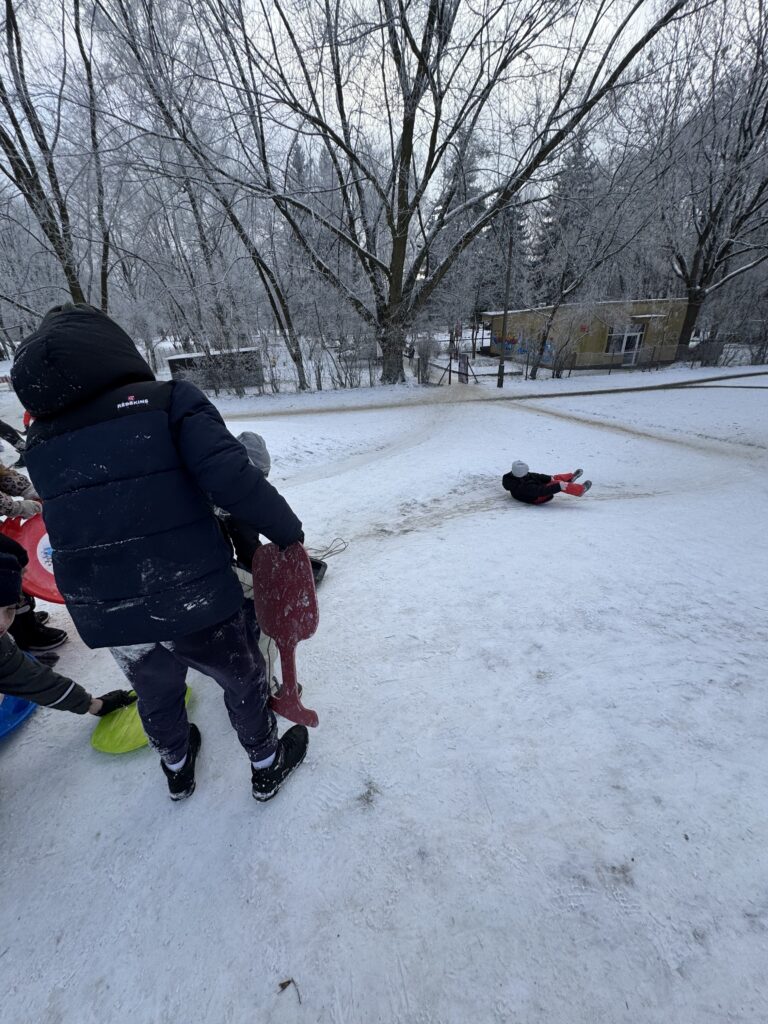 Uczniowie klasy 4b podczas wfu na śniegu zjeżdżają z górki.