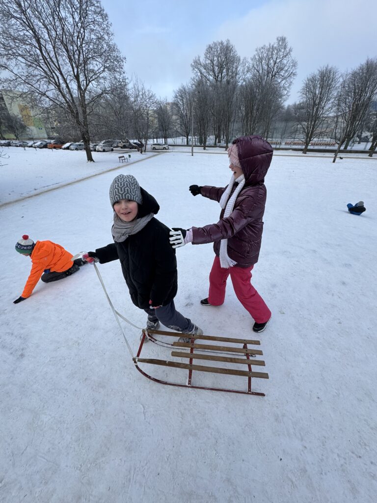 Uczniowie klasy 4b podczas wfu na śniegu zjeżdżają z górki.