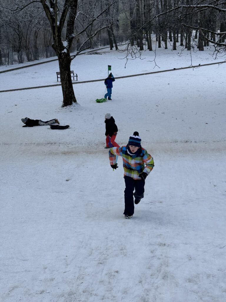 Uczniowie klasy 4b podczas wfu na śniegu zjeżdżają z górki.