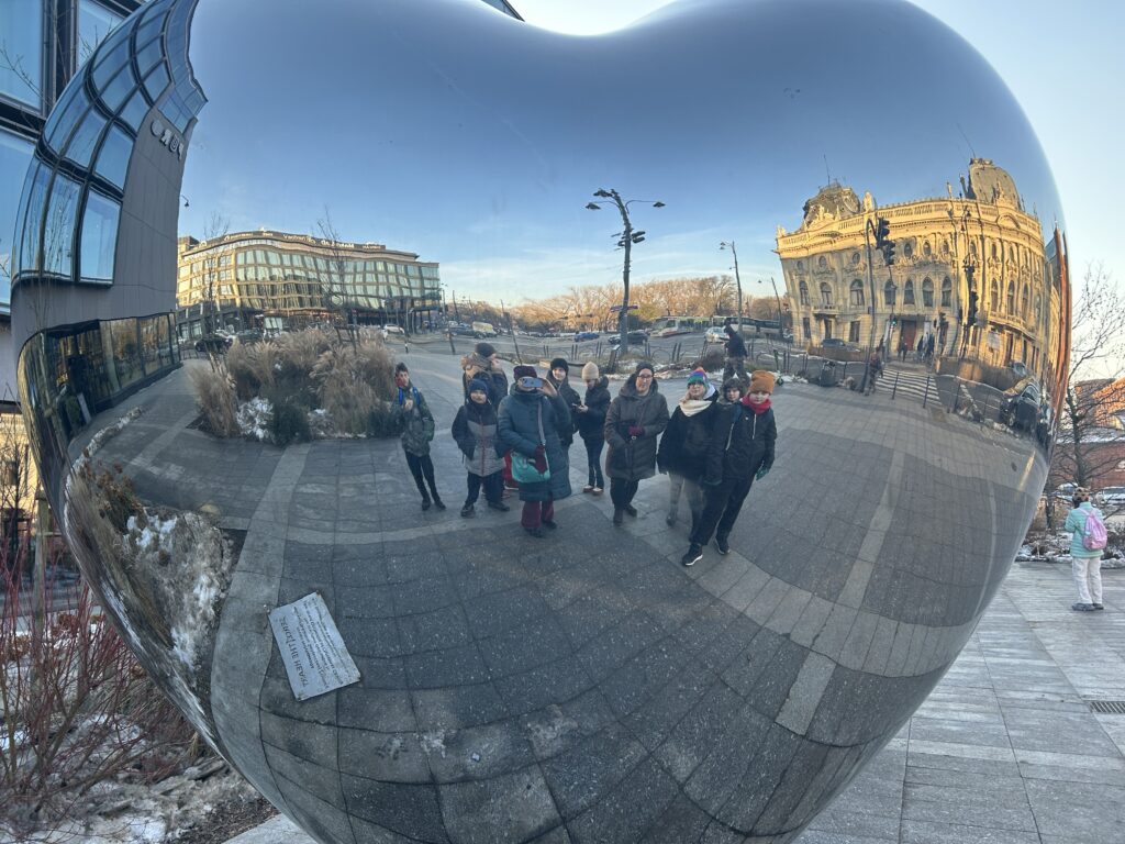 na placu WOŚP znajduje się ogromne szklane serce. Uczniowie i nauczycielki stoją przed nim i oglądając się w nim, robią zdjęcie. W sercu odbija się także Pałac Poznańskich