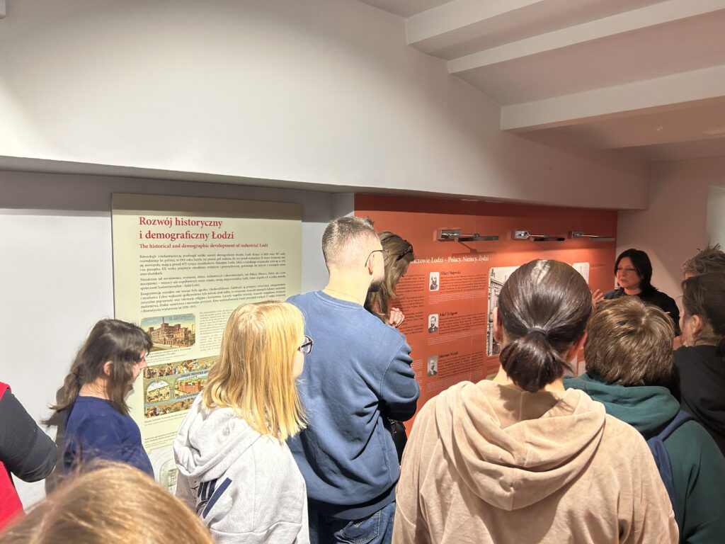 dzieci i osoby dorosłe stoją przed panią przewodnik i oglądają plansze nt. Rozwoju historycznego i demograficznego Łodzi