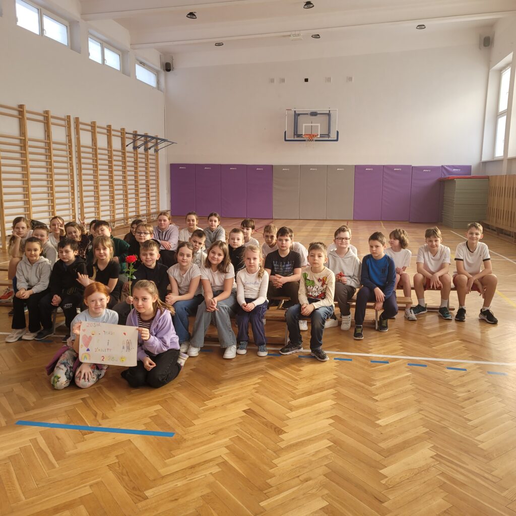 zdjęcie grupowe uczniów w sali gimnastycznej siedzą na ławkach