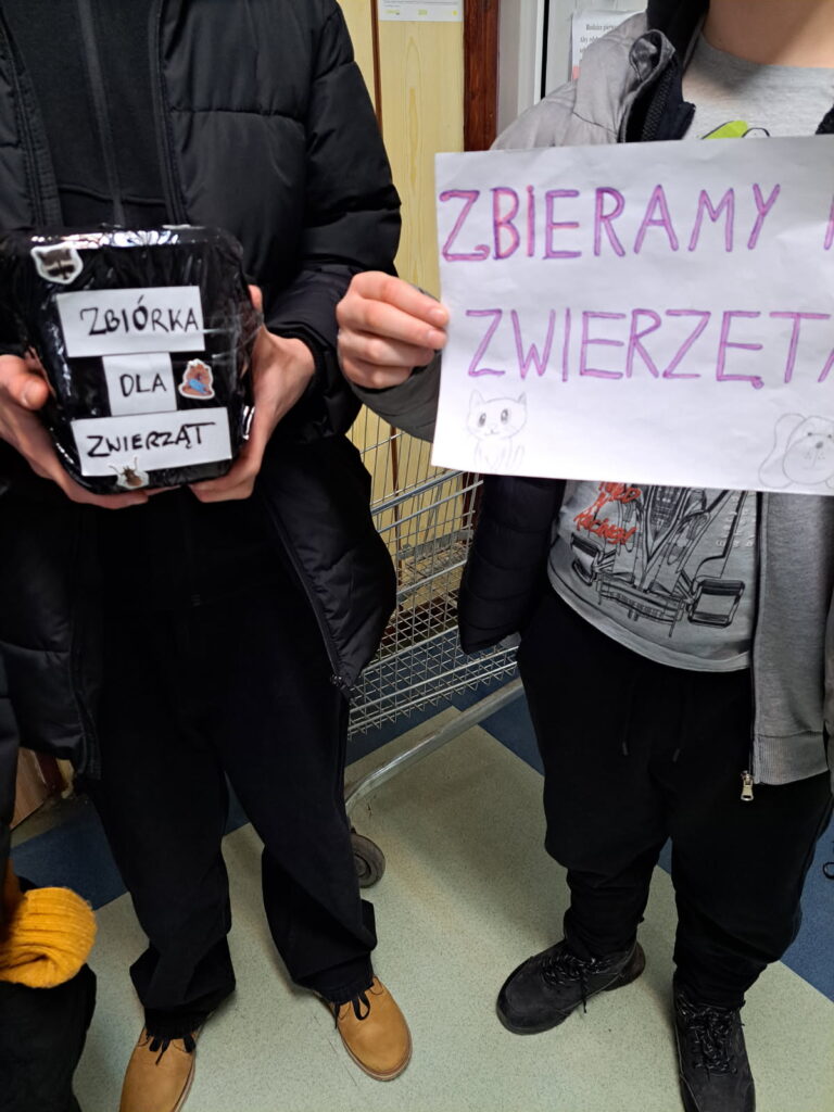 -dwaj chłopcy zbierają pieniądze dla zwierzaków. Jeden ma w ręku kartkę z napisem zbieramy na zwierzęta, drugi ma puszkę z napisem zbiórka dla zwierząt