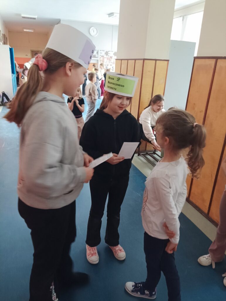 dzieci przeprowadzają ankietę na korytarzu, na głowie mają przepaski z napisem Dzień Bezpiecznego Internetu
