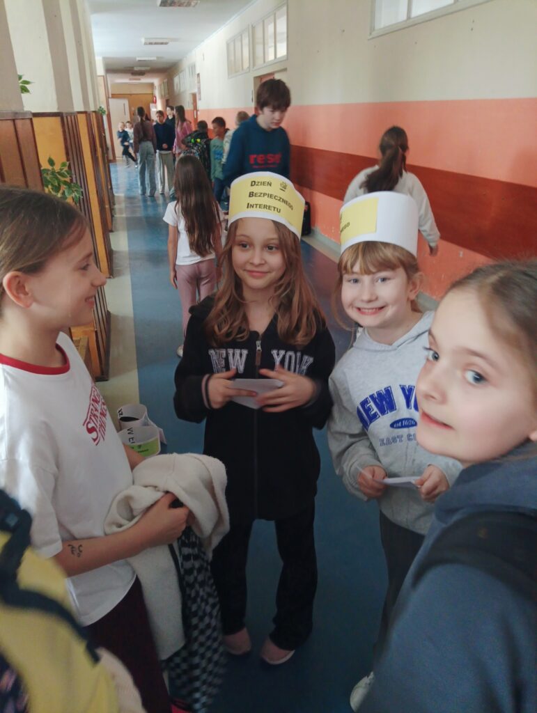 dzieci przeprowadzają ankietę na korytarzu, na głowie mają przepaski z napisem Dzień Bezpiecznego Internetu