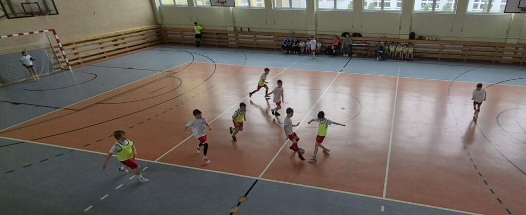 uczniowie grają w piłkę nożną na hali, drużyny w żółtych i białych koszulkach