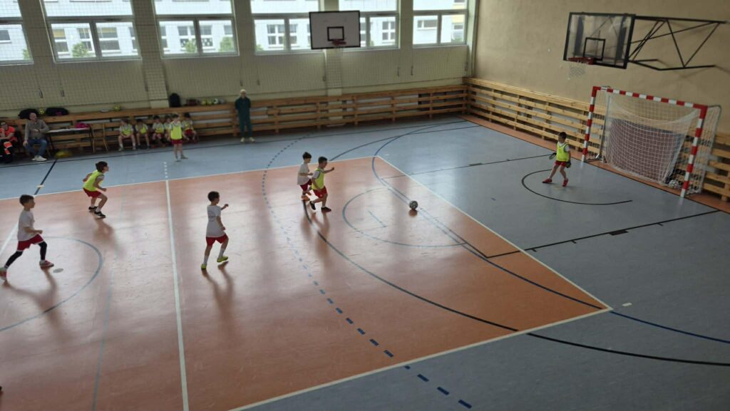 uczniowie grają w piłkę nożną na hali, drużyny w żółtych i białych koszulkach