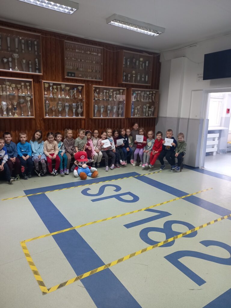 przedszkolaki siedzą na ławkach nad nimi puchary