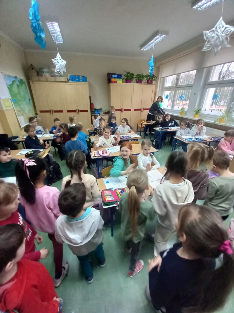 przedszkolaki rozmawiają z dziećmi siedzącymi w ławkach w klasie