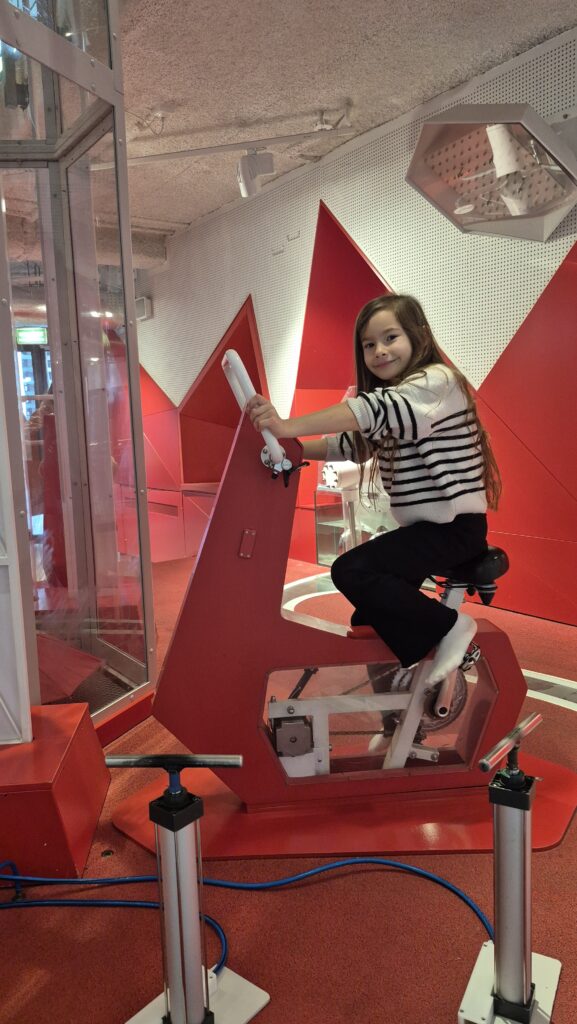 Uczennica siedzi na czerwonym rowerku.