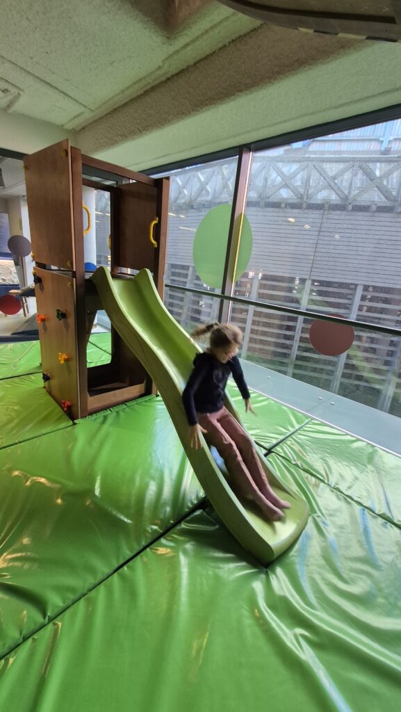 Uczennica zjeżdża na zielonej zjeżdżalni.