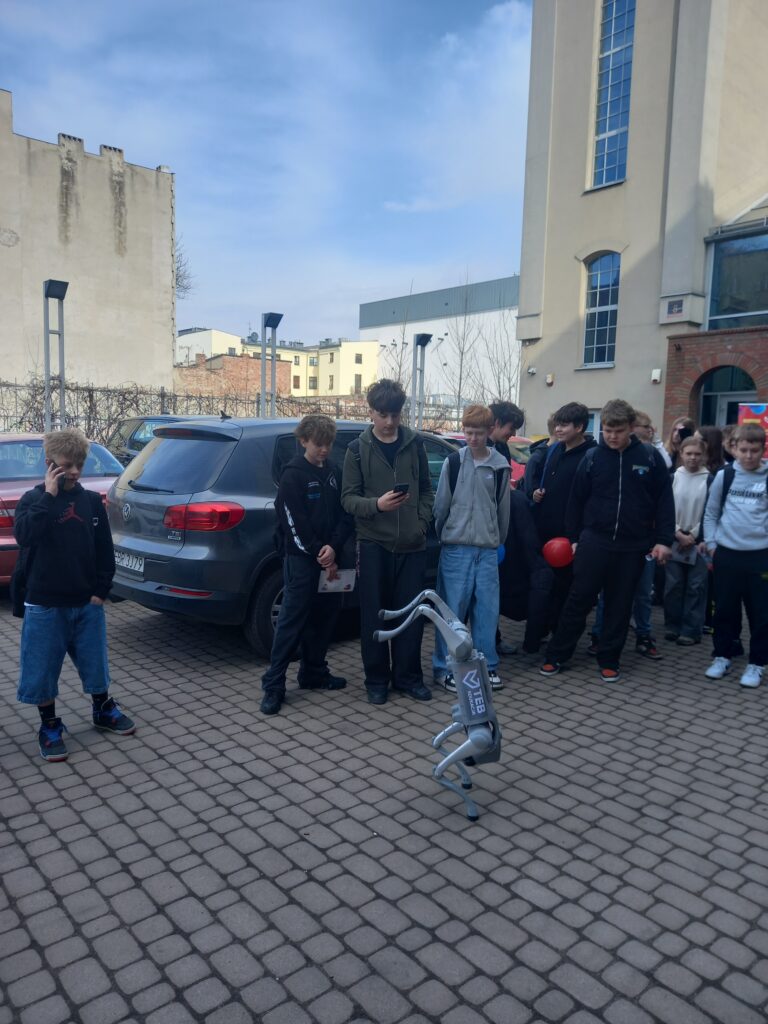 uczniowie stoją i patrzą na robota, jeden z nich go fotografuje 