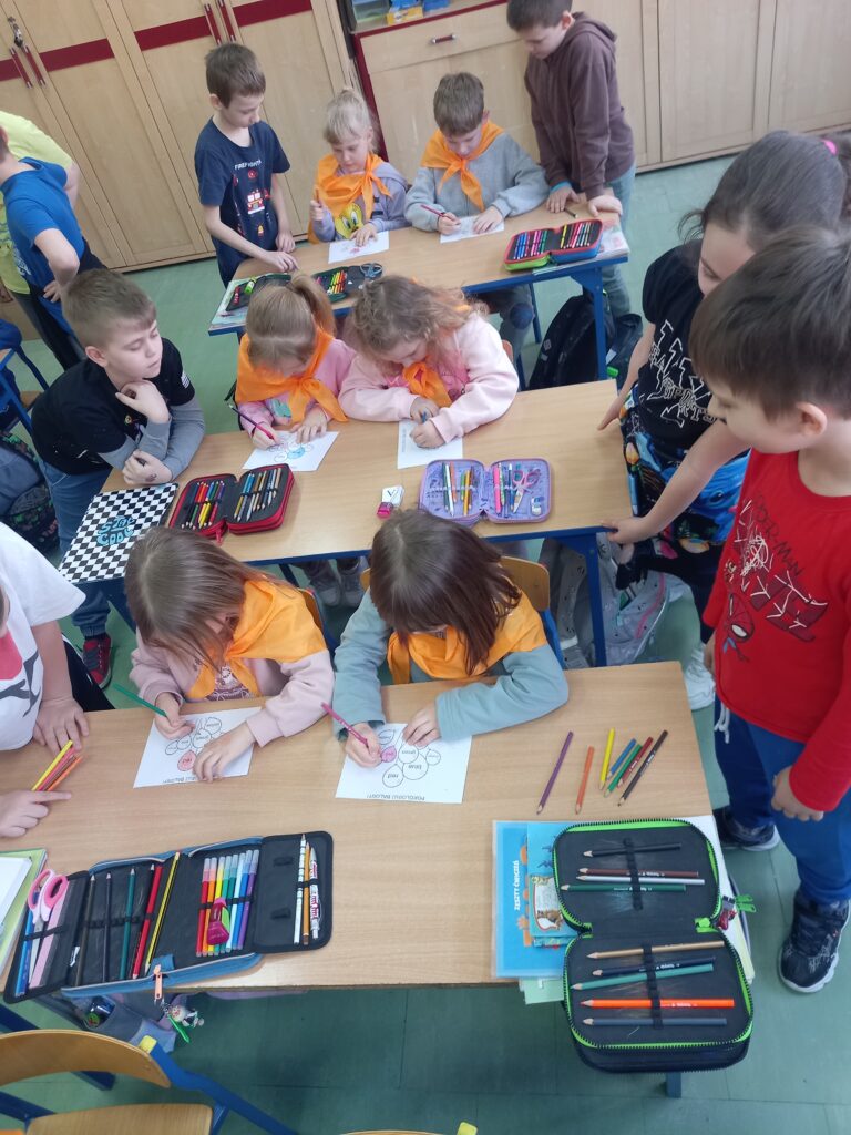 przedszkolaki  wykonuja zadania w ławkach, przy nich stoją uczniowie