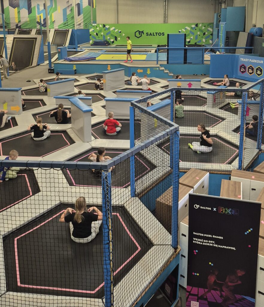 Uczniowie 4a wykonują ćwiczenia rozciągające na trampolinach pod okiem prowadzącego.