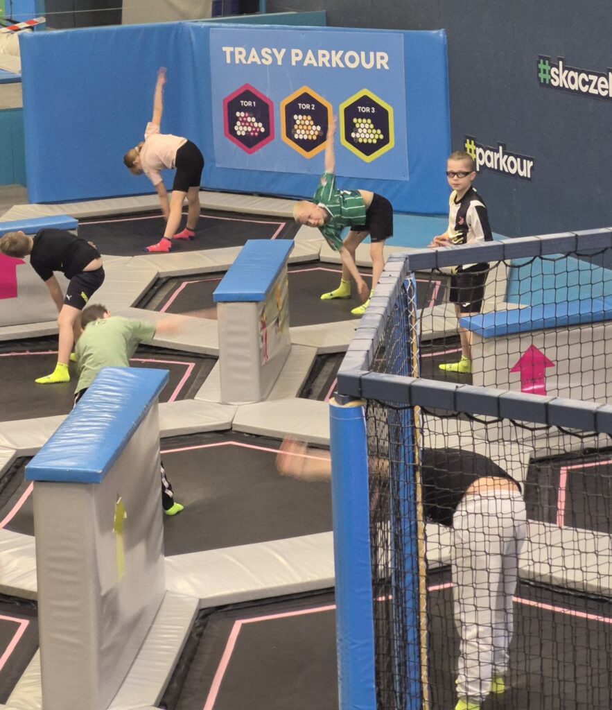 Uczniowie 4a wykonują ćwiczenia rozciągające na trampolinach pod okiem prowadzącego.