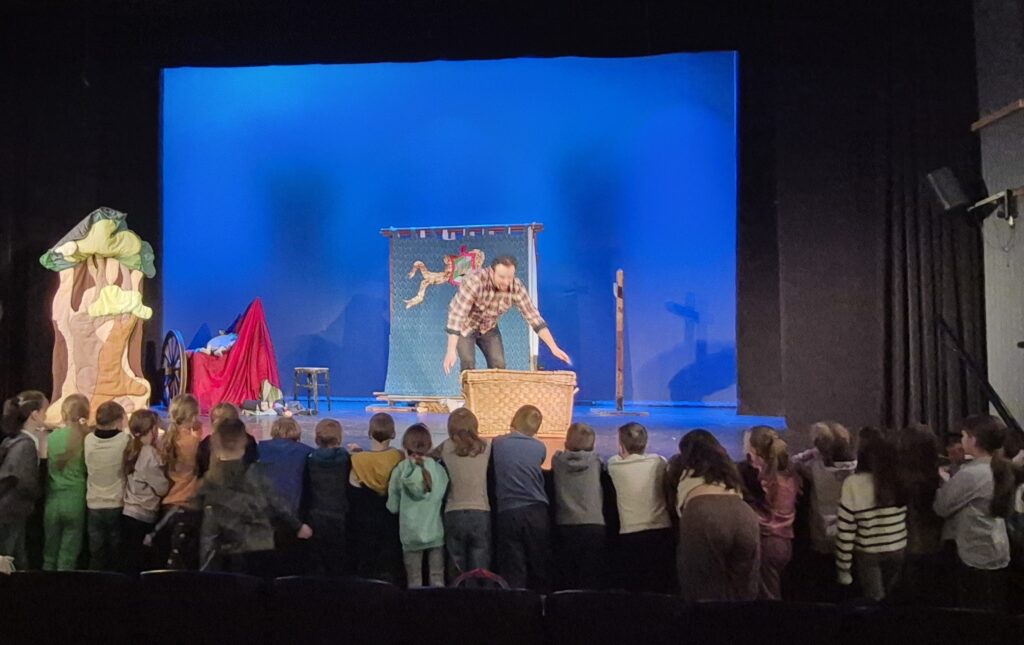 aktor pochyla się ku dzieciom stojącym przy scenie