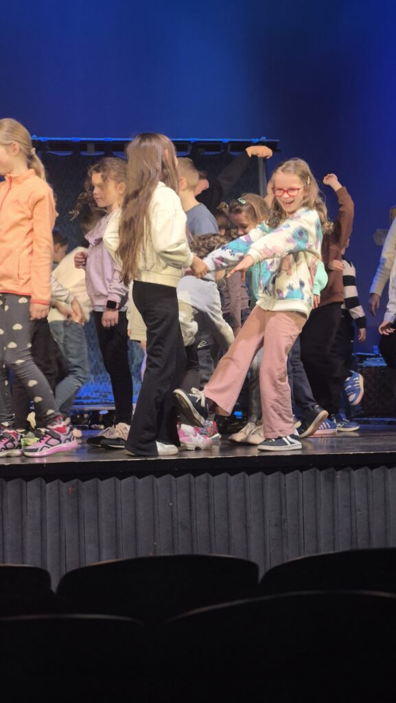 dzieci stoją na scenie, trzymają się za ręce, uśmiechają 
