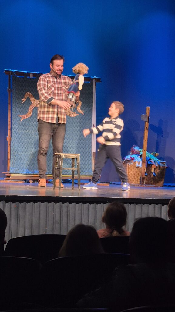 aktor trzyma kukiełkę, obok stoi chłopczyk i patrzy na niego