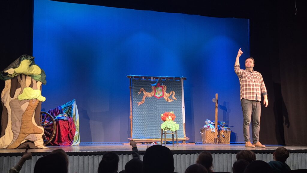 na scenie widać kukiełkę w zielonym ubranku i czerwonych włosach