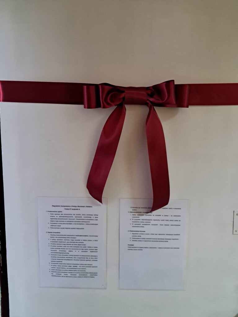 Zdjęcie przedstawia wejście do Pokoju Wyciszeń w budynku A szkoły. Drzwi udekorowano wstęgą. Na drzwiach zawieszono regulamin korzystania z Pokoju.