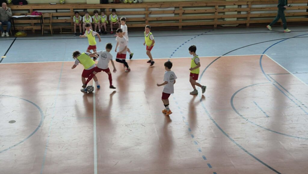 uczniowie grają w piłkę nożną na hali, drużyny w żółtych i białych koszulkach