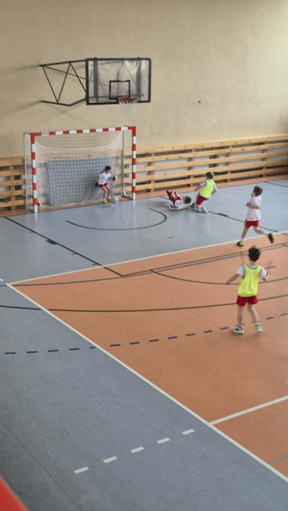 uczniowie grają w piłkę nożną na hali, drużyny w żółtych i białych koszulkach