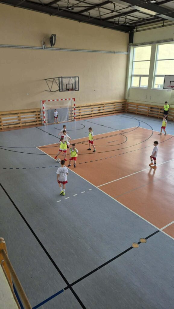 uczniowie grają w piłkę nożną na hali, drużyny w żółtych i białych koszulkach