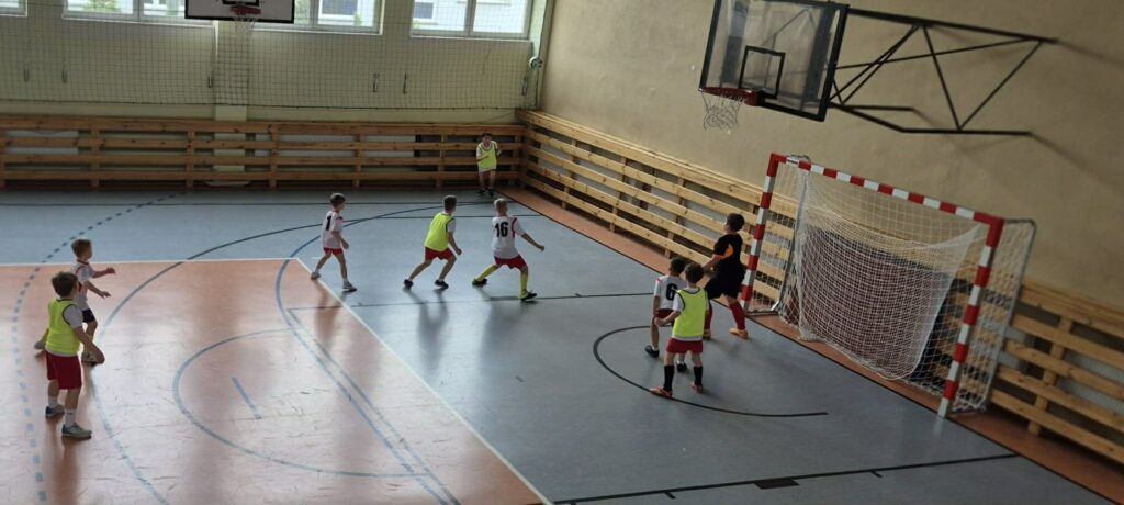 uczniowie grają w piłkę nożną na hali, drużyny w żółtych i białych koszulkach