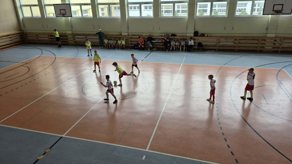 uczniowie grają w piłkę nożną na hali, drużyny w żółtych i białych koszulkach