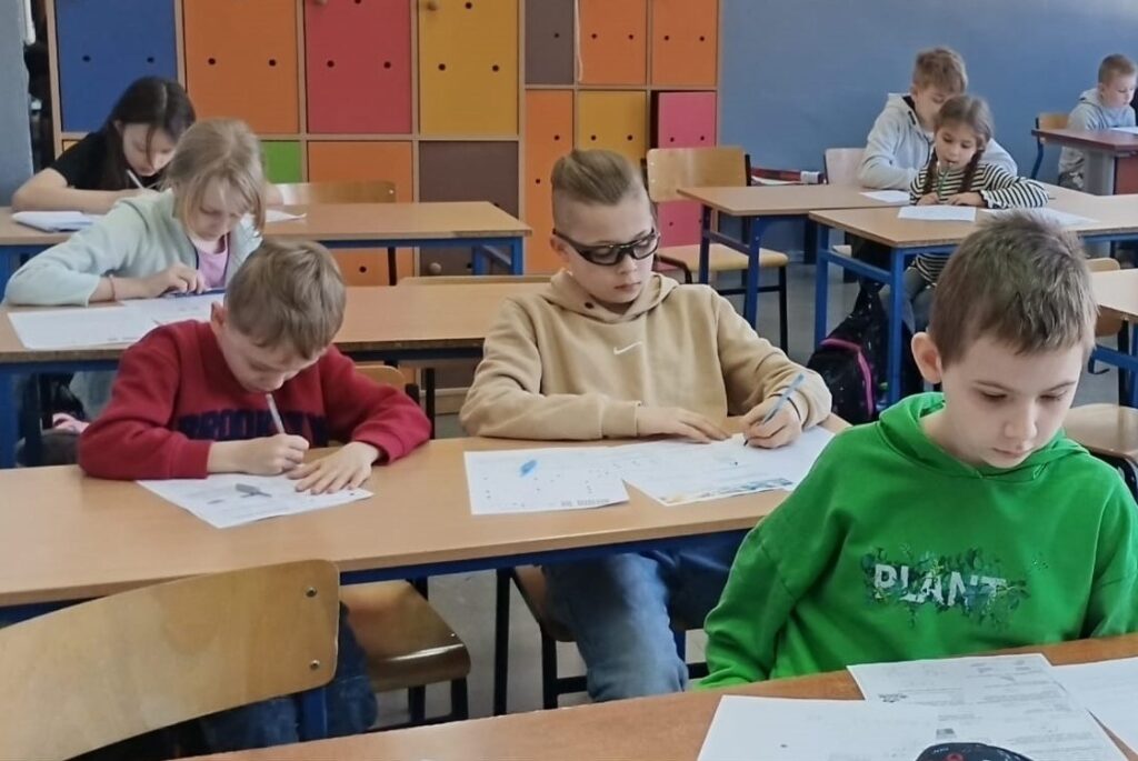 Uczniowie siedzą w klasie w ławkach nad arkuszami konkursowymi.