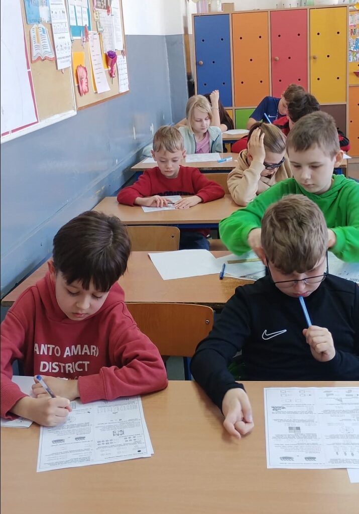 Uczniowie siedzą w klasie w ławkach nad arkuszami konkursowymi.